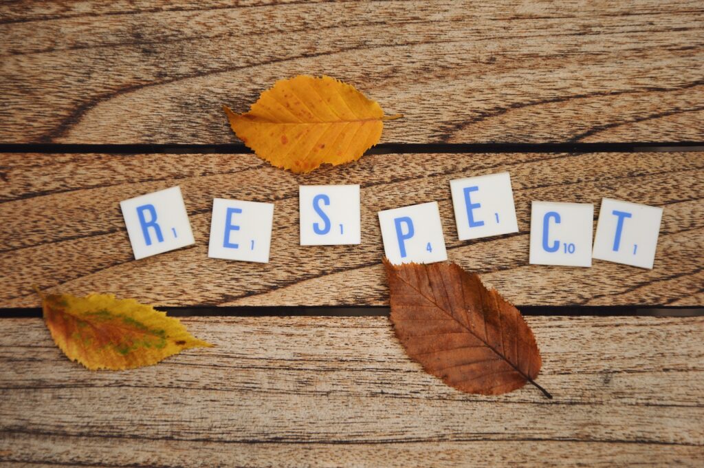 Overhead photo of letters or text saying respect and autumn leaves on a wooden tabble