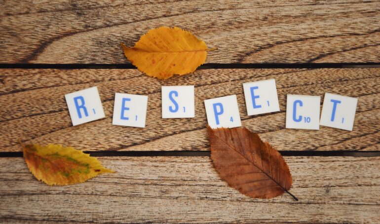 Overhead photo of letters or text saying respect and autumn leaves on a wooden tabble