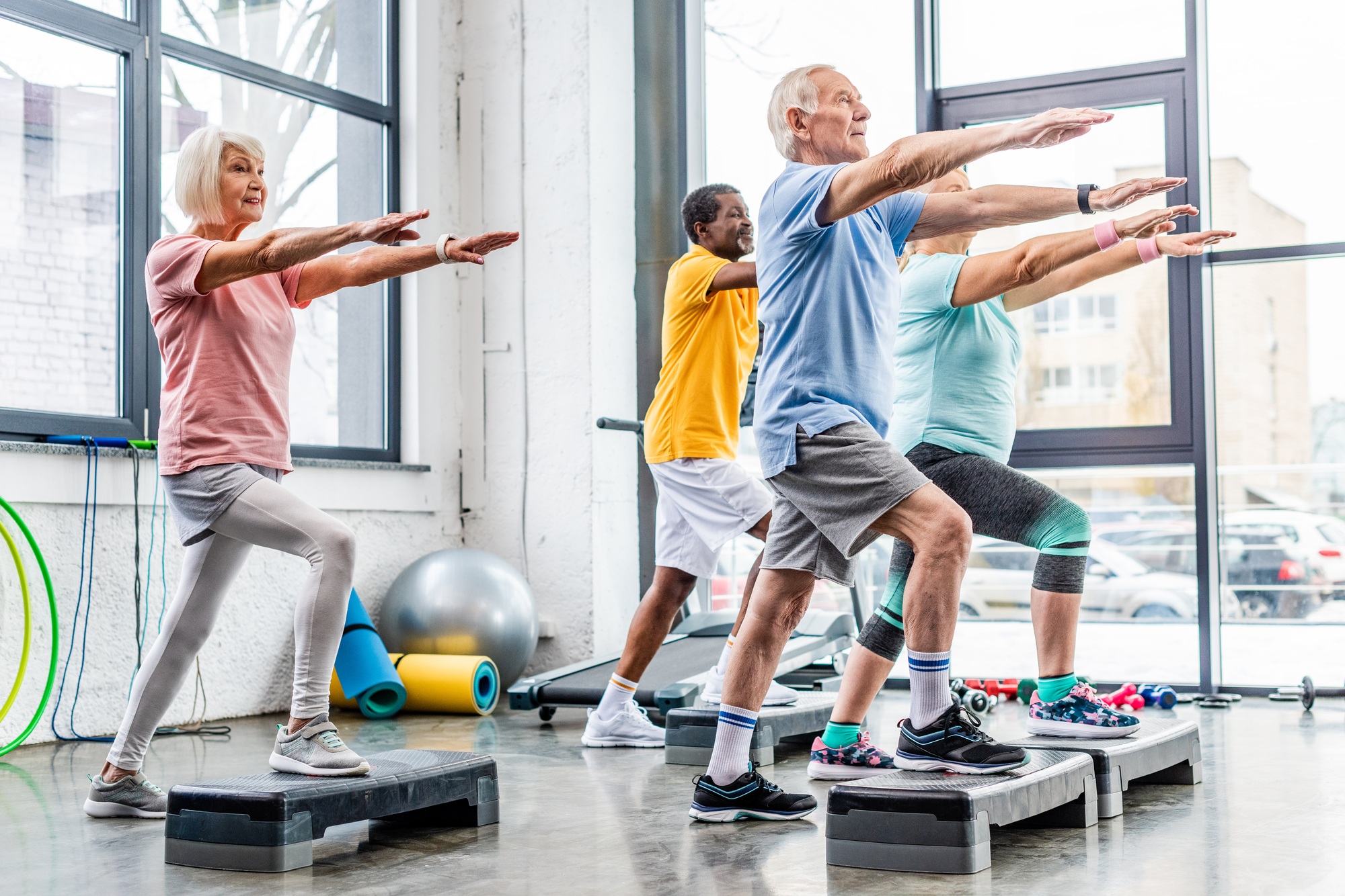 senior athletes synchronous exercising on step platforms at gym